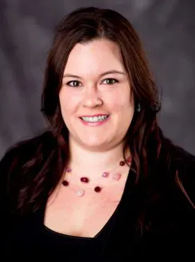 Smiling woman in a black top and pink necklace against a dark gray backdrop