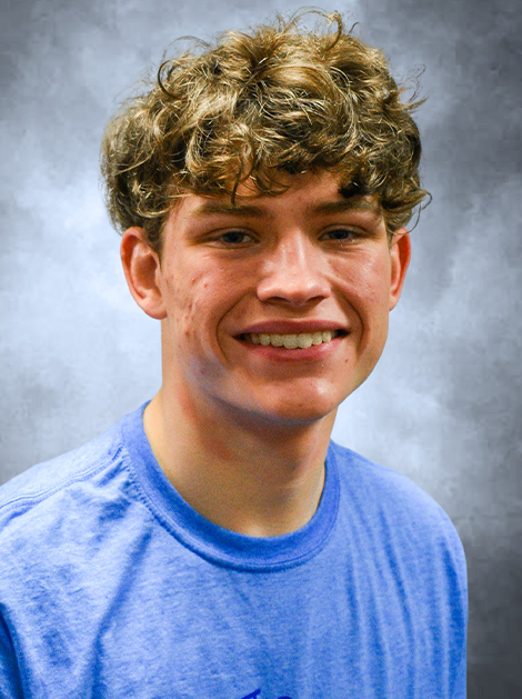 Smiling person in a blue shirt against a gray studio backdrop