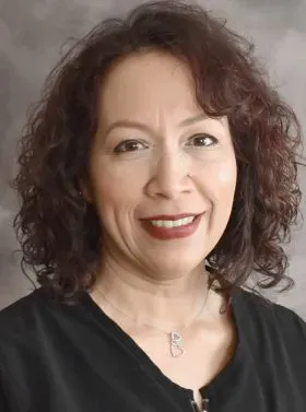 Studio portrait of a smiling woman with curly dark hair in a black top and silver necklace