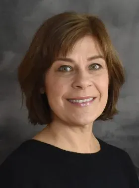 Portrait of a smiling woman in a black top against a gray studio backdrop
