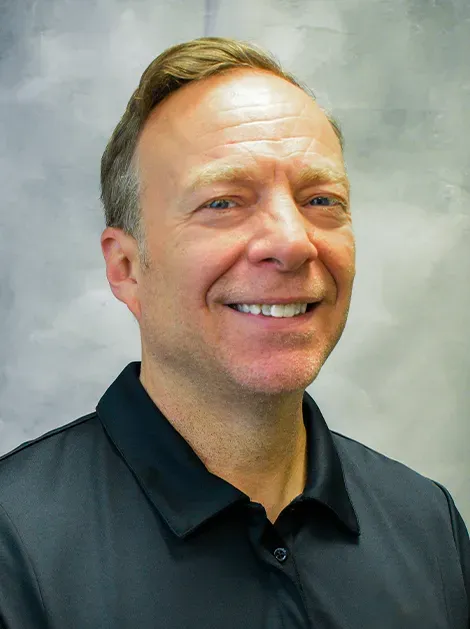 Man smiling in a dark polo shirt against a light gray background