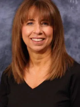 Smiling woman with shoulder-length brown hair wearing a black top against a gray studio backdrop