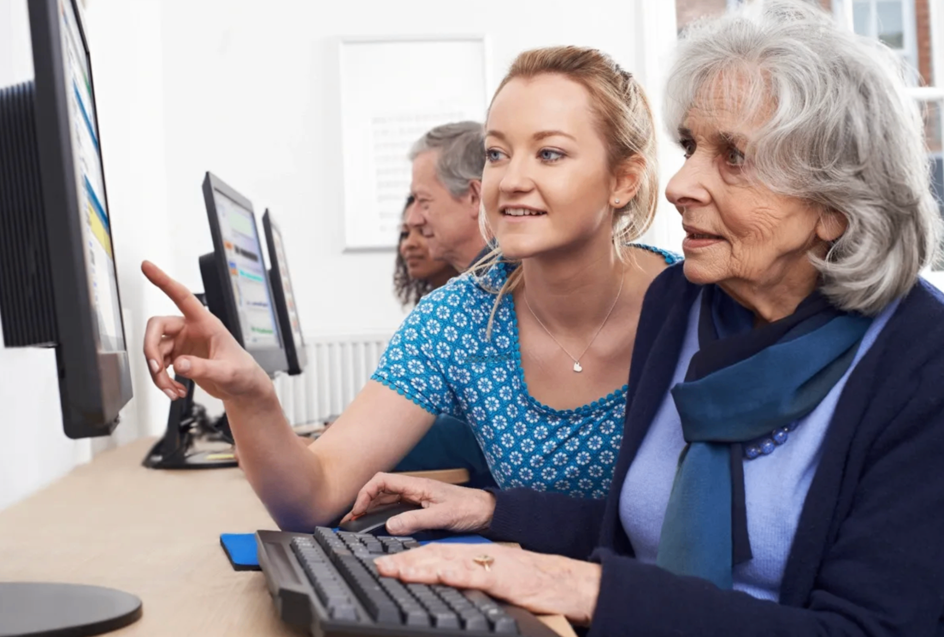 Three people using a computer at a desk, one pointing at the screen and smiling.