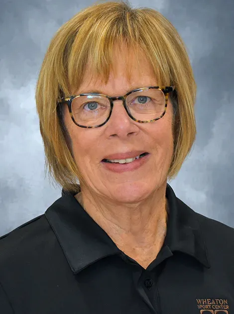 Portrait of a smiling person with glasses in a black collared shirt against a gray background