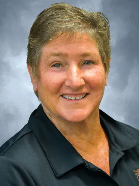 Smiling person in a dark polo shirt against a soft blue-gray studio background