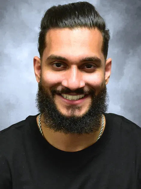 Smiling man with dark hair and beard against a gray studio backdrop