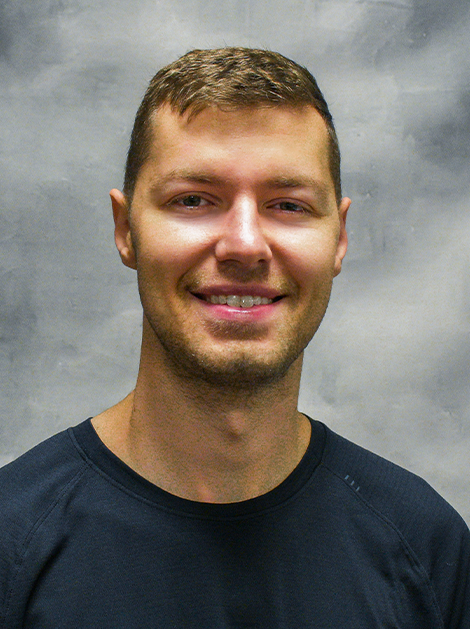 Smiling man in a dark shirt against a gray studio backdrop