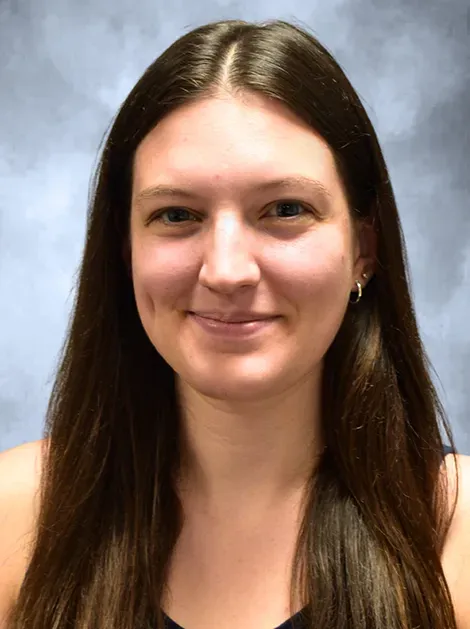 Smiling woman with long dark hair against a blue-gray studio backdrop