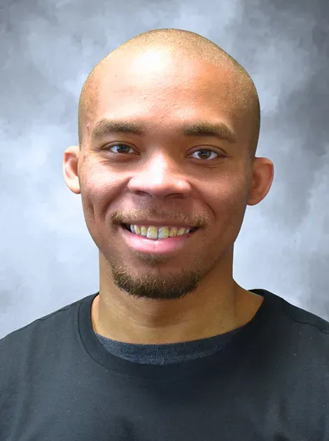 Smiling bald man with a goatee wearing a black shirt against a gray background