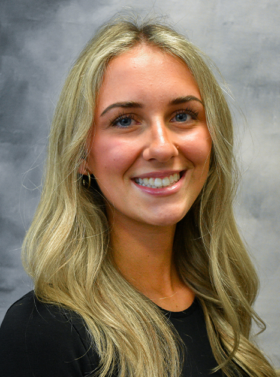 Smiling blonde person in a black top against a gray studio background