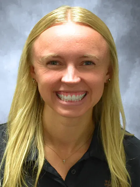 Smiling person with long blonde hair in a black shirt against a gray background