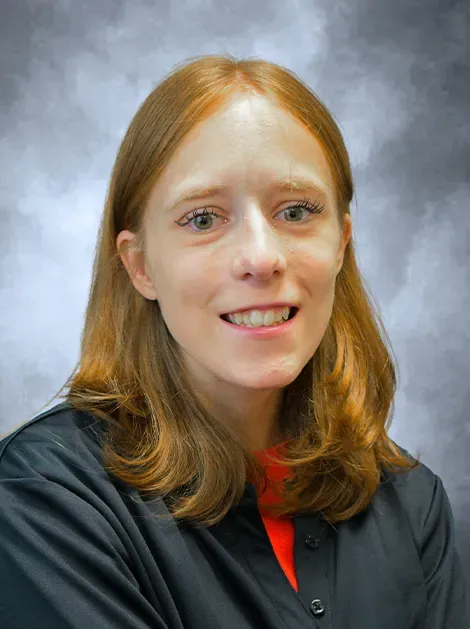Portrait of a woman with red hair in a dark shirt against a gray studio backdrop