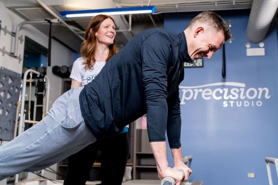 Two people doing Pilates exercises on reformer machines in a studio
