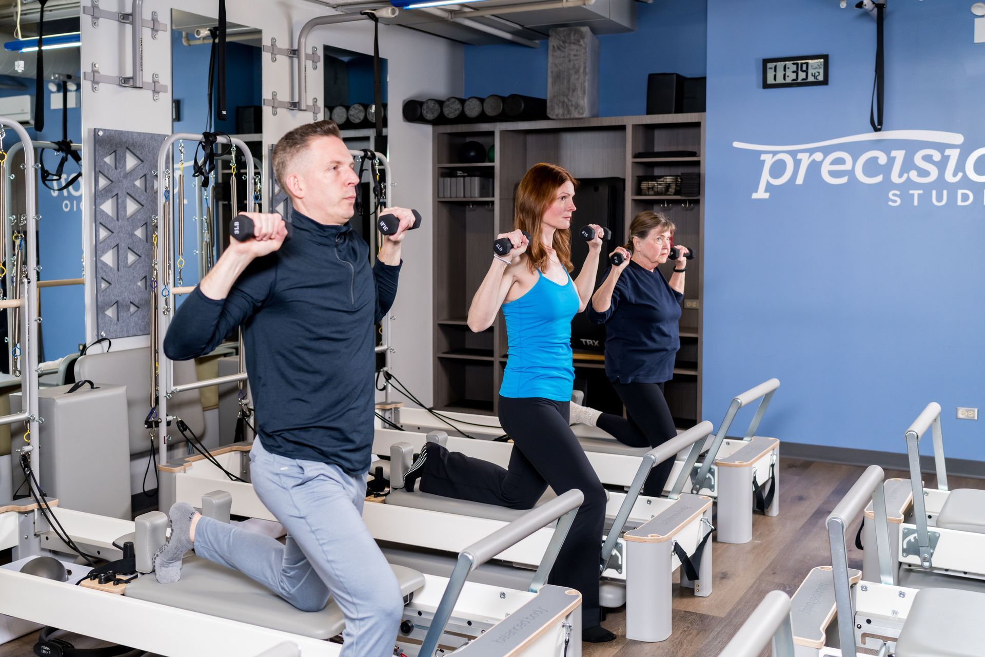People exercising on Pilates reformers in a bright studio with blue walls