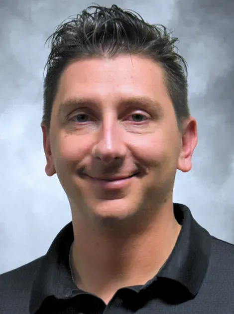 Headshot of a smiling person in a black polo shirt against a gray backdrop