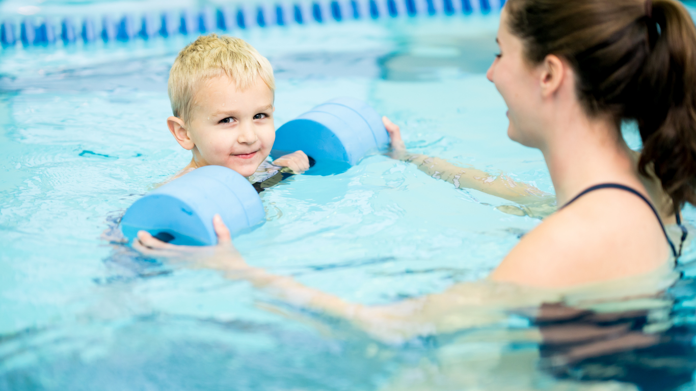 Adult assisting child in a swimming pool, holding a blue float ring