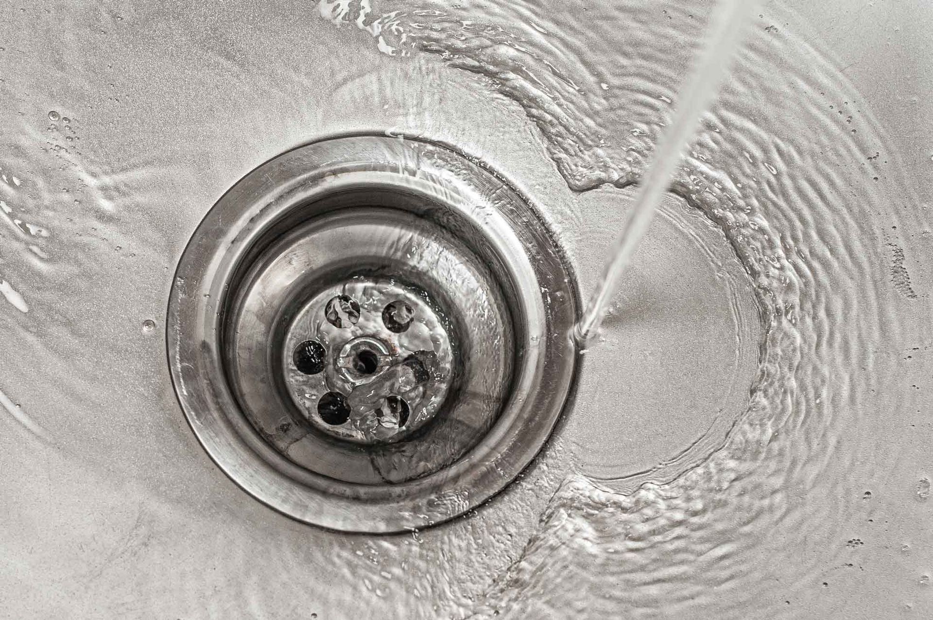 Water flowing into a clean stainless steel kitchen sink drain Water flowing into a clean stainless steel kitchen sink drain