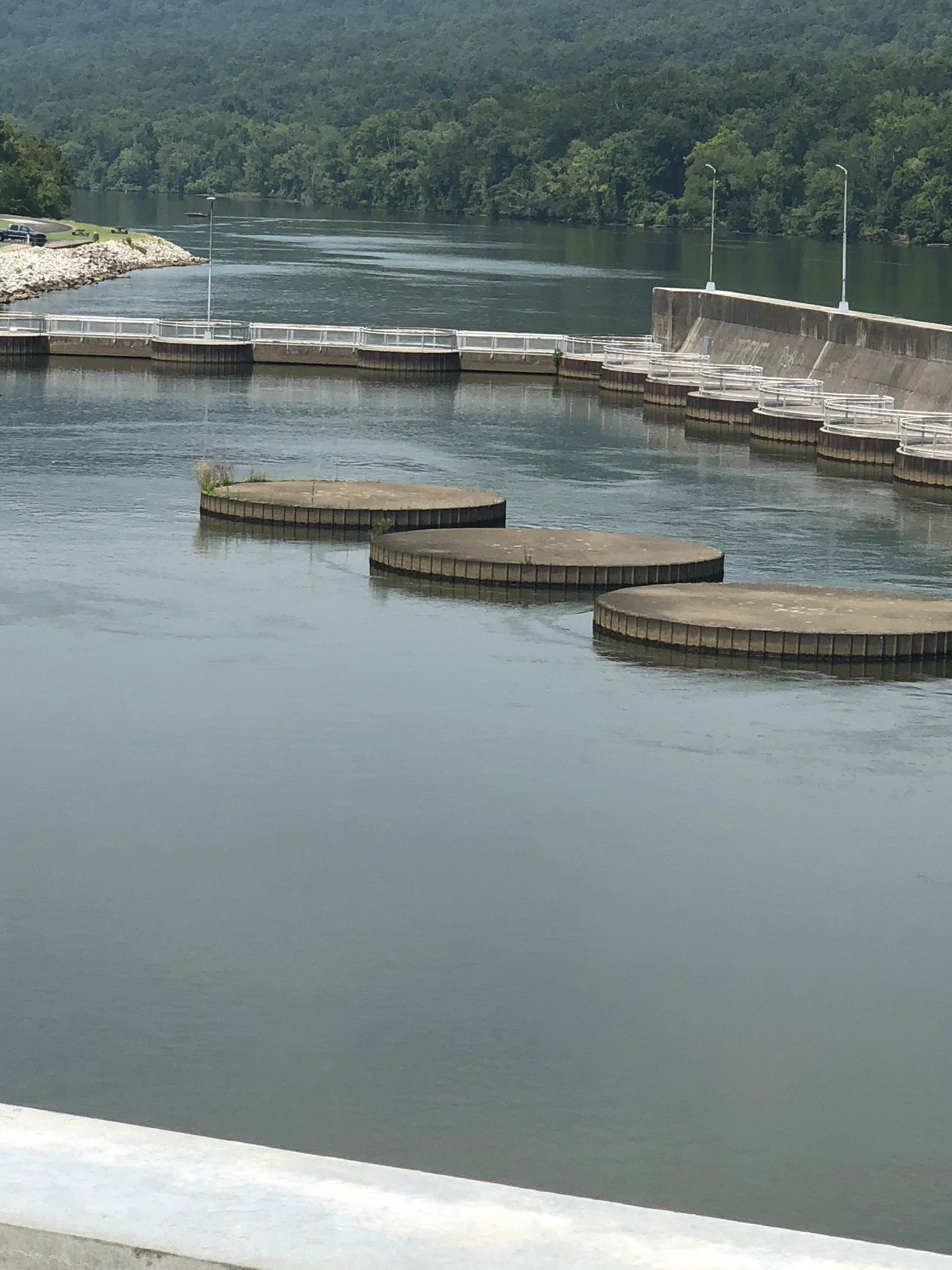River with concrete platforms and a dam, trees in background.
