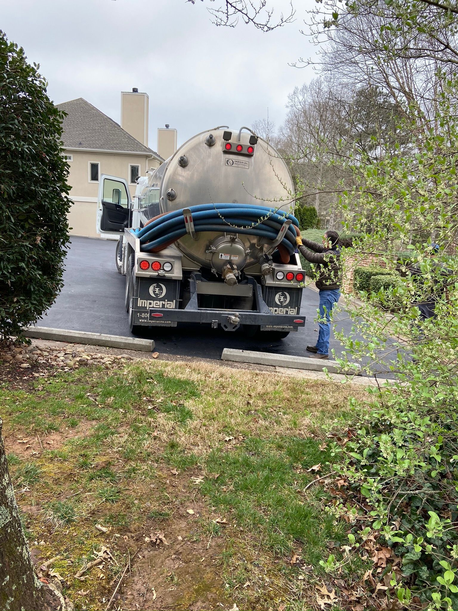 Septic tank truck parked in front of a house. A worker is attending to the hoses.