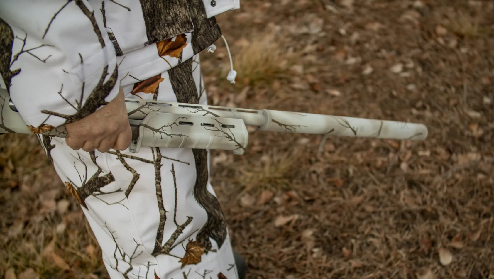 Person in white camouflage holding a shotgun in a wooded area.