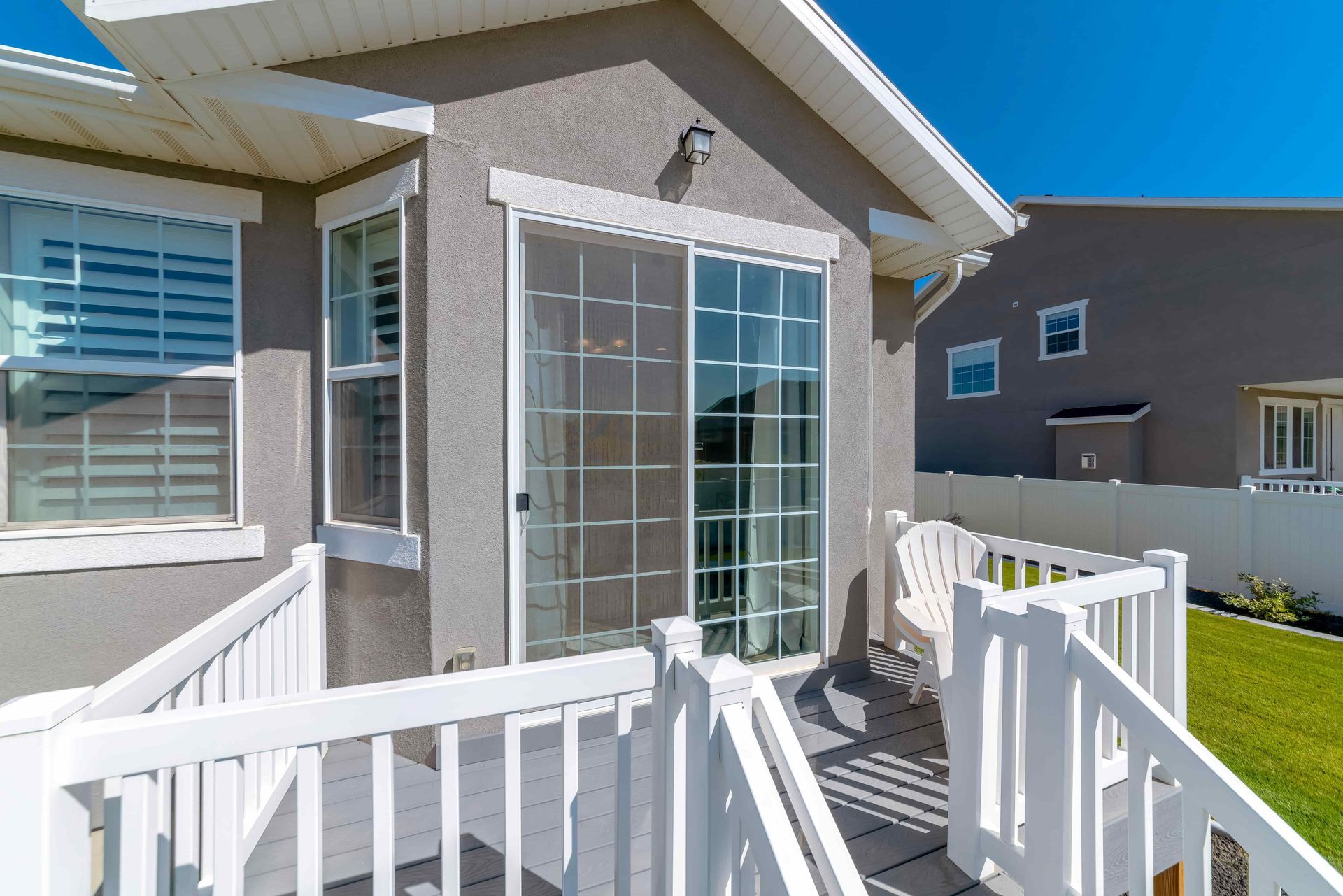 Back patio with white railings, sliding glass door, and beige house exterior under a bright blue sky