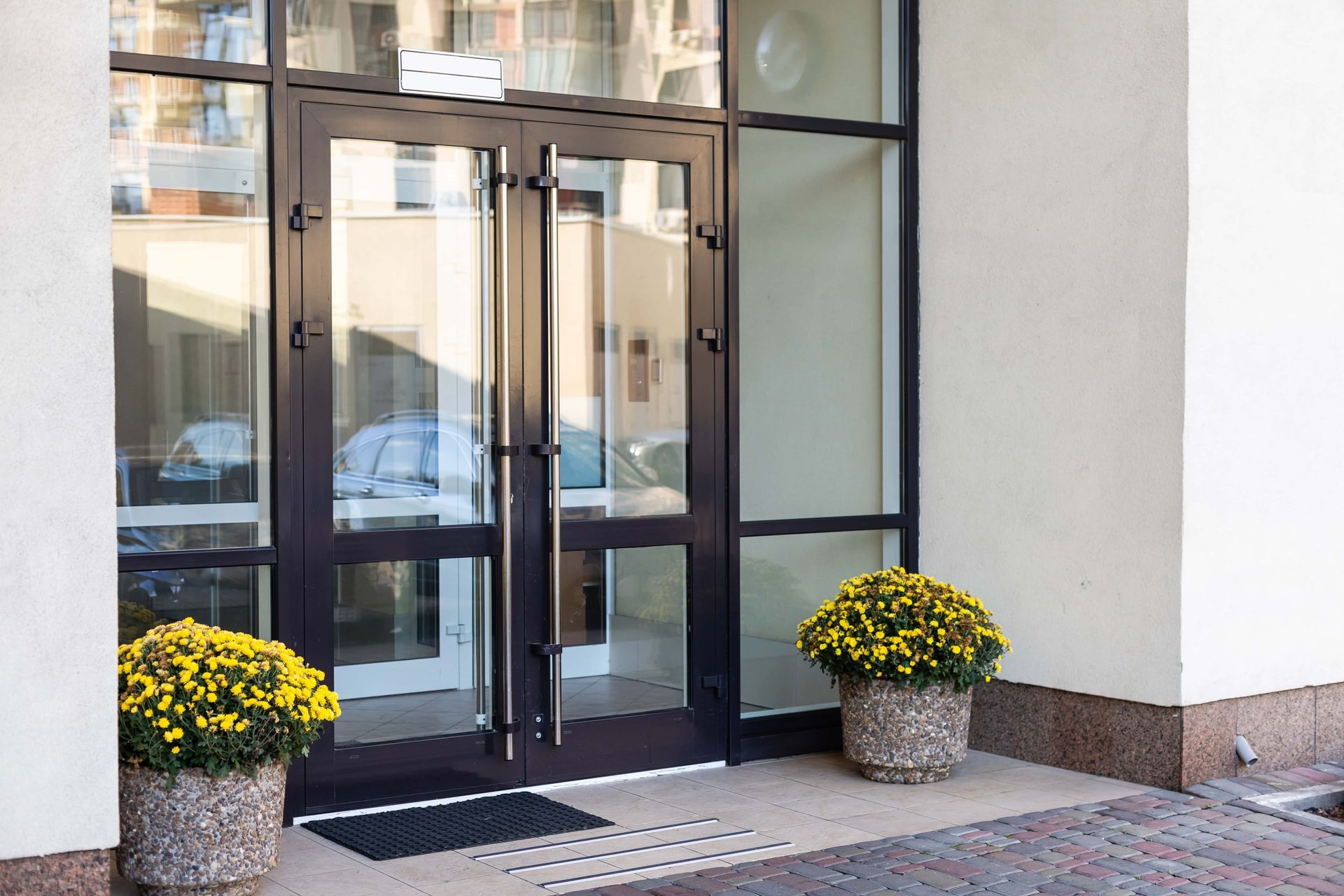 Glass storefront entrance with double doors and two potted yellow flowers outside