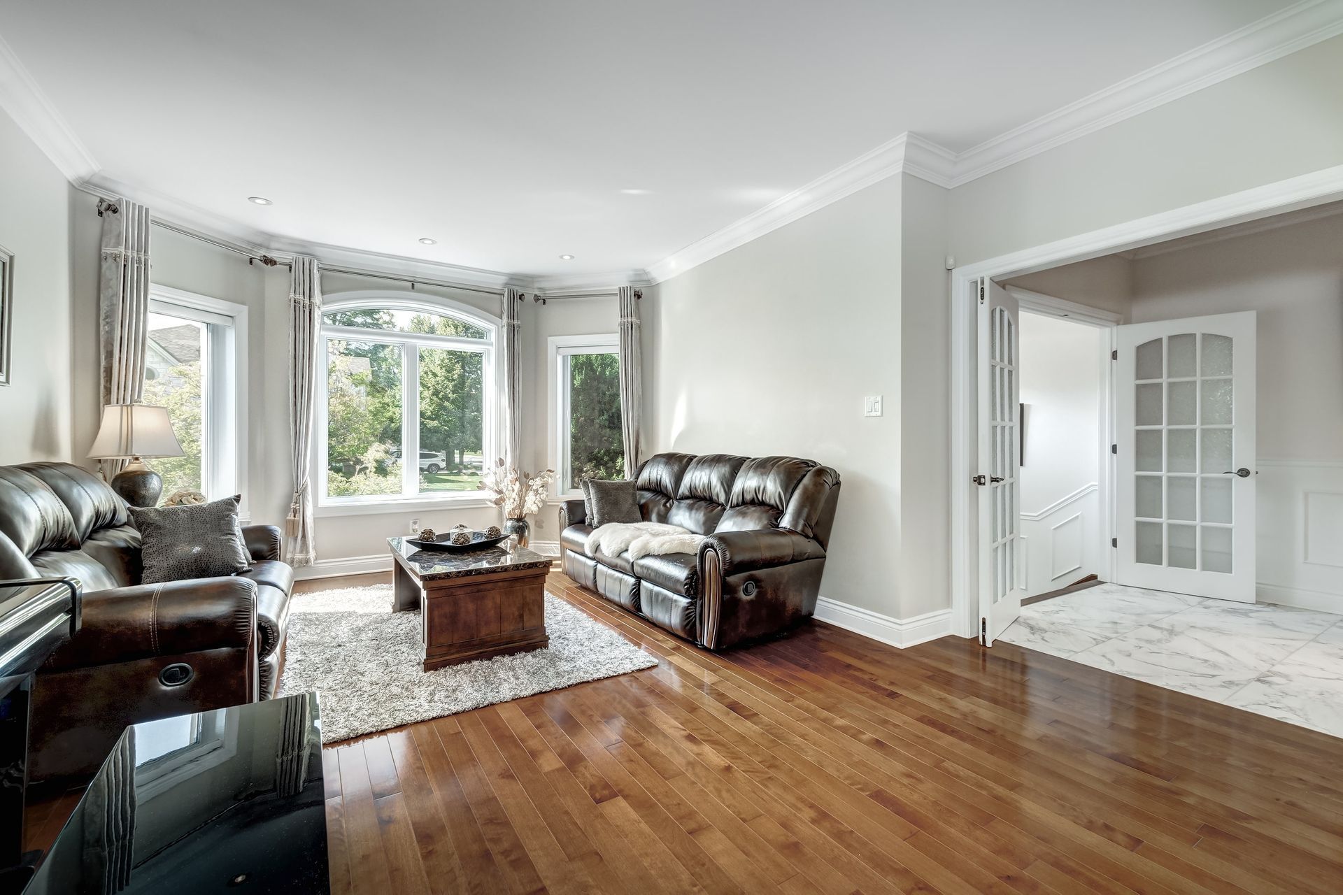 Bright living room with leather sofas, coffee table, bay windows, and hardwood floors