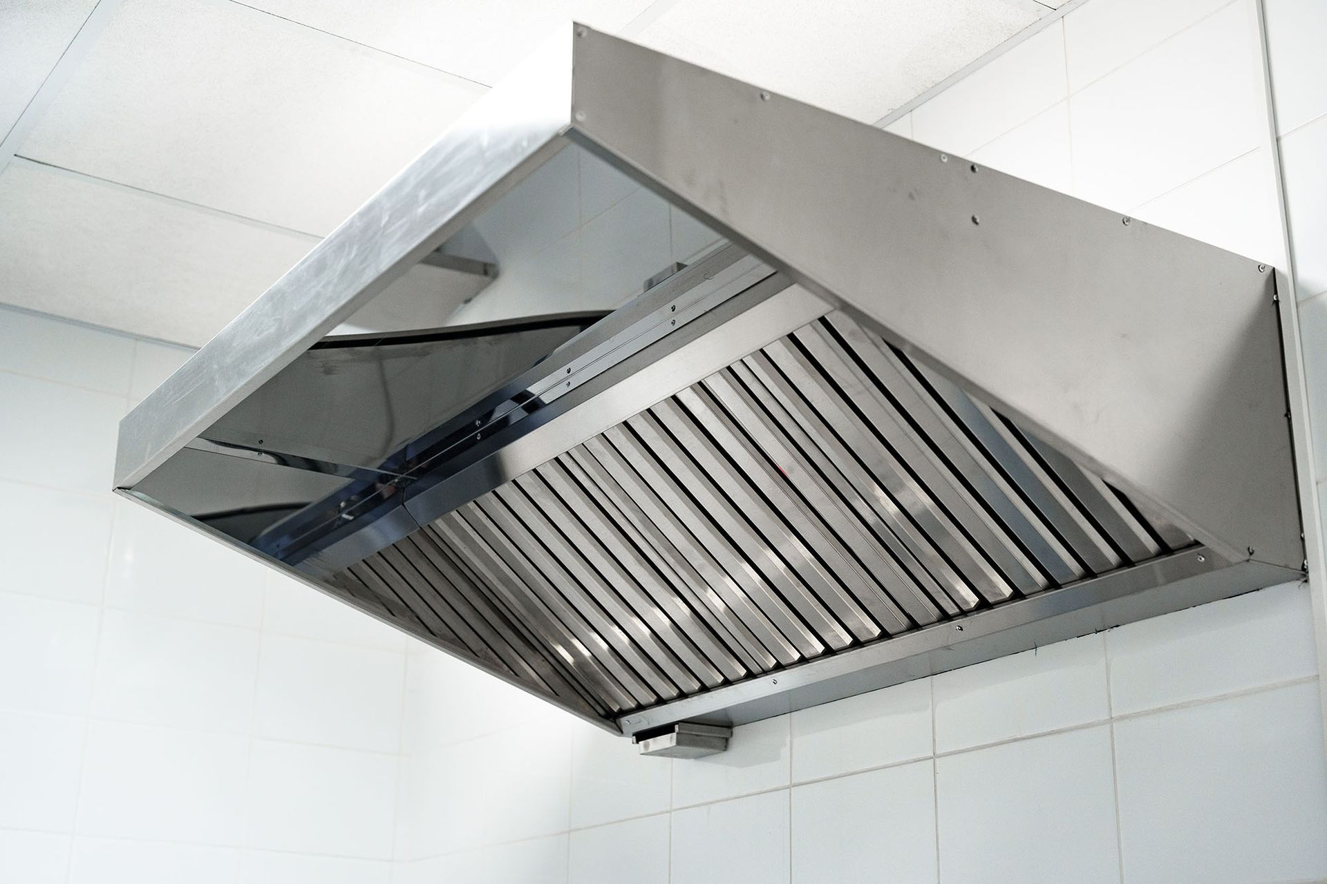 Stainless steel kitchen range hood with vent filters mounted against white tiled wall