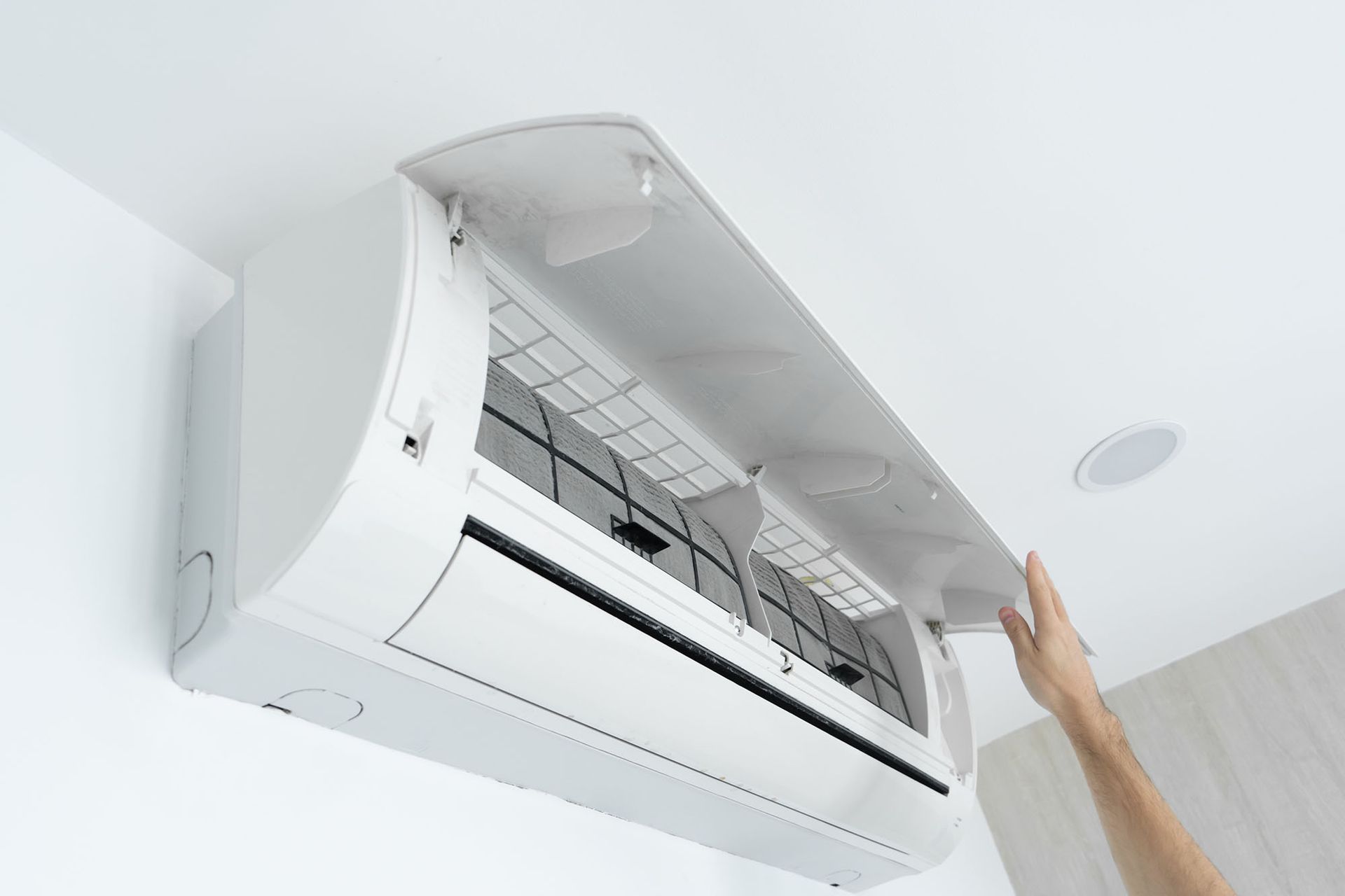 Hand opening a wall-mounted air conditioner with a lifted front cover and visible filter.