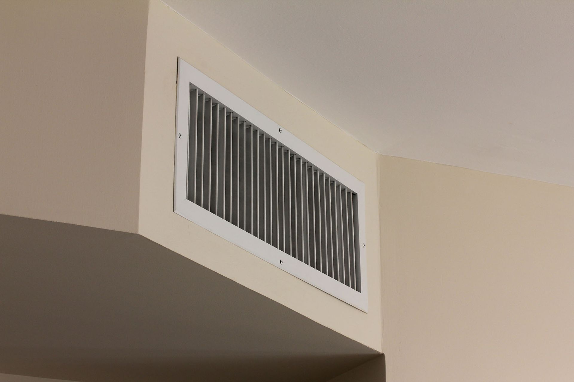 White wall vent near the ceiling on a beige interior wall
