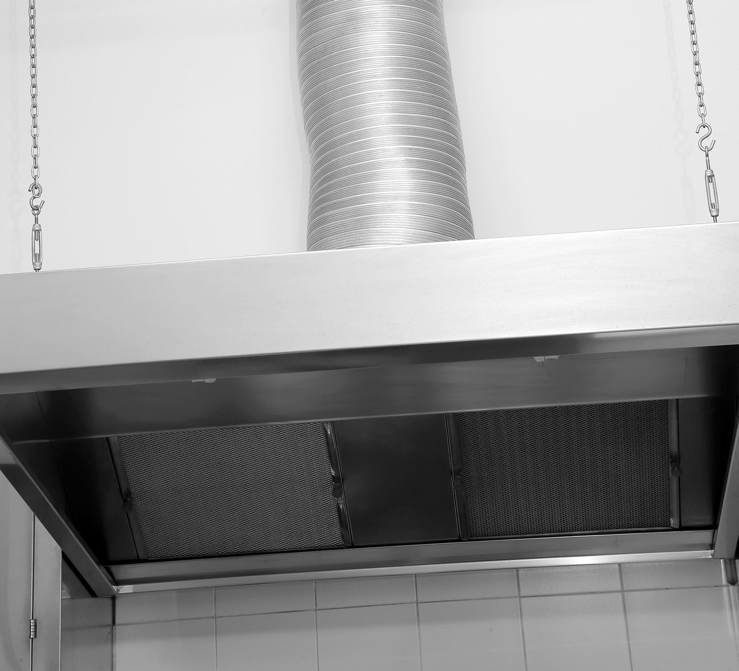 Black-and-white view of a kitchen range hood and vent with tiled wall below.