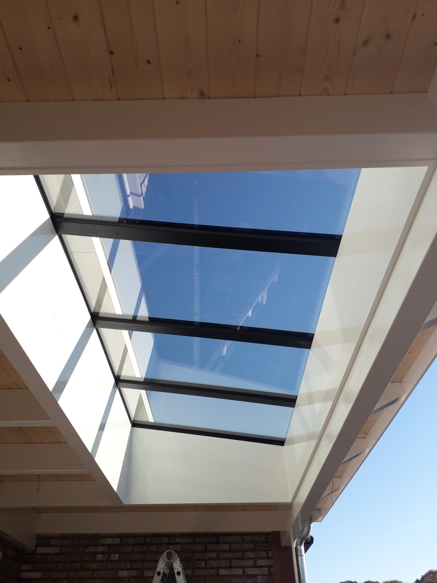 Dakraam met uitzicht op de blauwe lucht door het houten plafond van een overdekt terras.