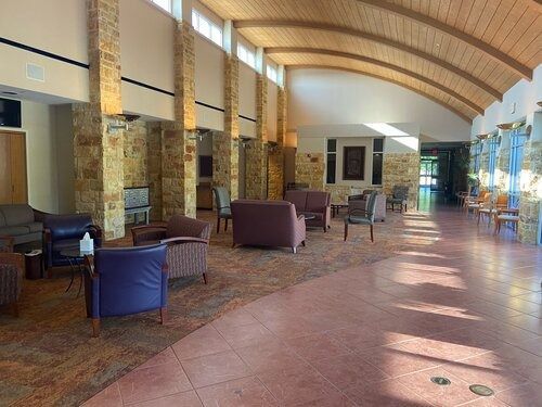 Covered outdoor lounge with wicker chairs, stone columns, and a curved wooden ceiling in warm sunlight