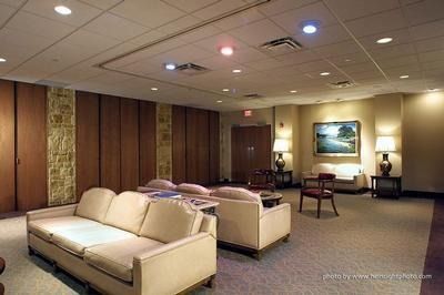 Spacious beige lounge with sofas, carpet, wood-paneled walls, and framed painting under recessed lighting