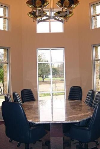 Conference room with oval table, black chairs, and tall windows centered on a glass door.