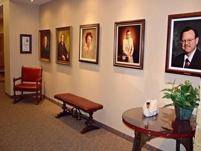 Hallway with framed portraits, a red chair, a wooden bench, and a round table with a plant and tissues.