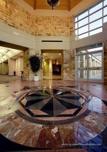 Bright hotel lobby with stone walls, marble floor, and a large compass mosaic centerpiece