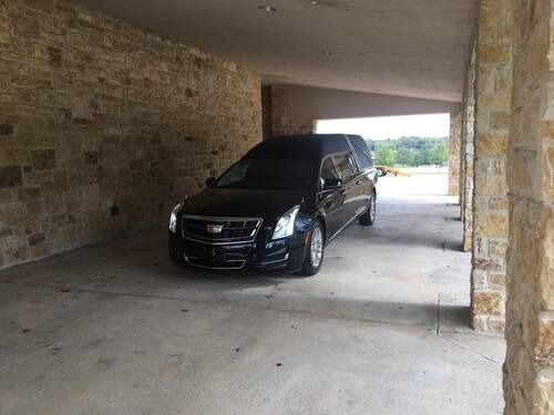 Black SUV parked in a stone carport, facing the camera with daylight visible beyond.