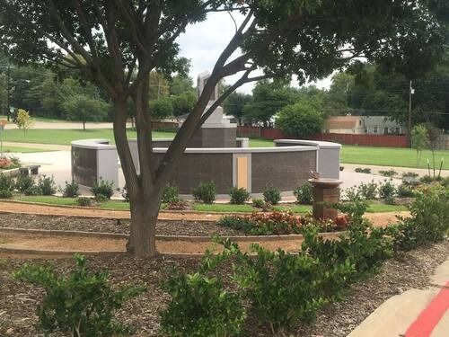 Tree in landscaped park with brick monument and flower beds near a sidewalk