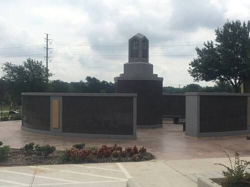 Outdoor memorial with curved black walls and a central stone monument in a paved plaza