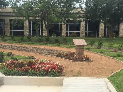 Landscaped courtyard with flower bed, stone plaque, and a building in the background