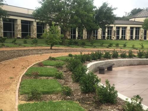 Curved courtyard path beside a circular bench and landscaped greenery in front of a building