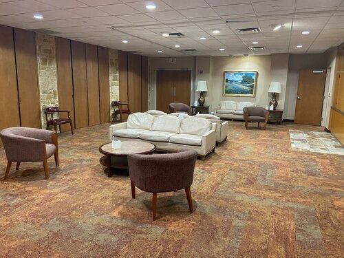 Spacious hotel lounge with white sofa, armchairs, wood-paneled walls, and patterned carpet.