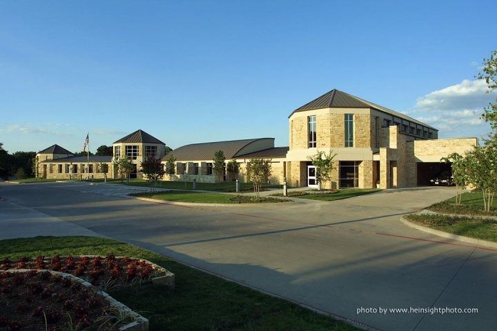 Wide view of a modern tan stone building complex with a driveway and blue sky