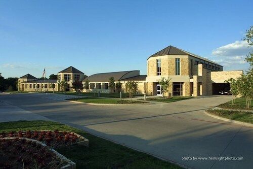 Large stone office building with a driveway, landscaped lawn, and clear blue sky