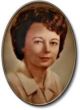 Oval-framed portrait of a person with short dark hair wearing a light collared blouse on a neutral background