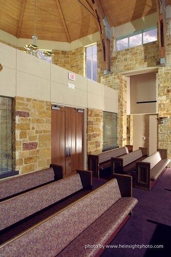 Empty church sanctuary with wooden pews, stone walls, and high vaulted ceiling