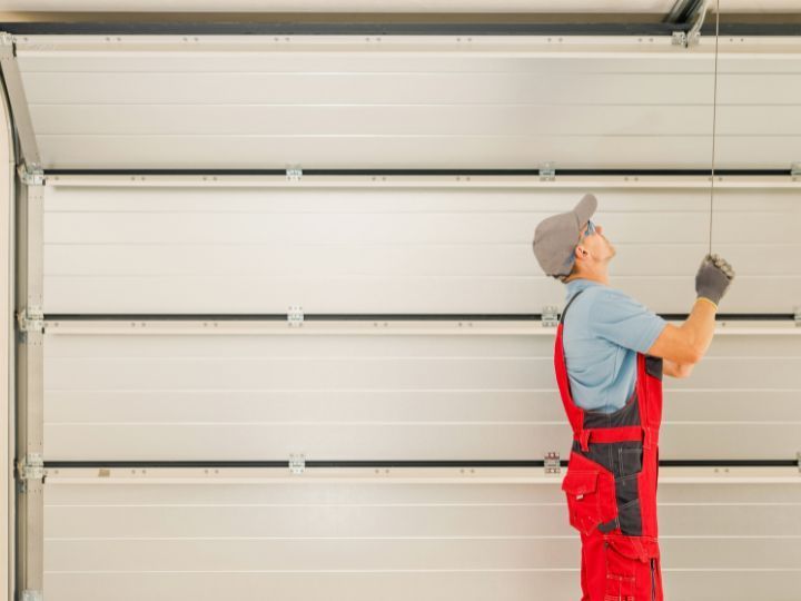 Worker in red overalls installing a garage door panel with a tool