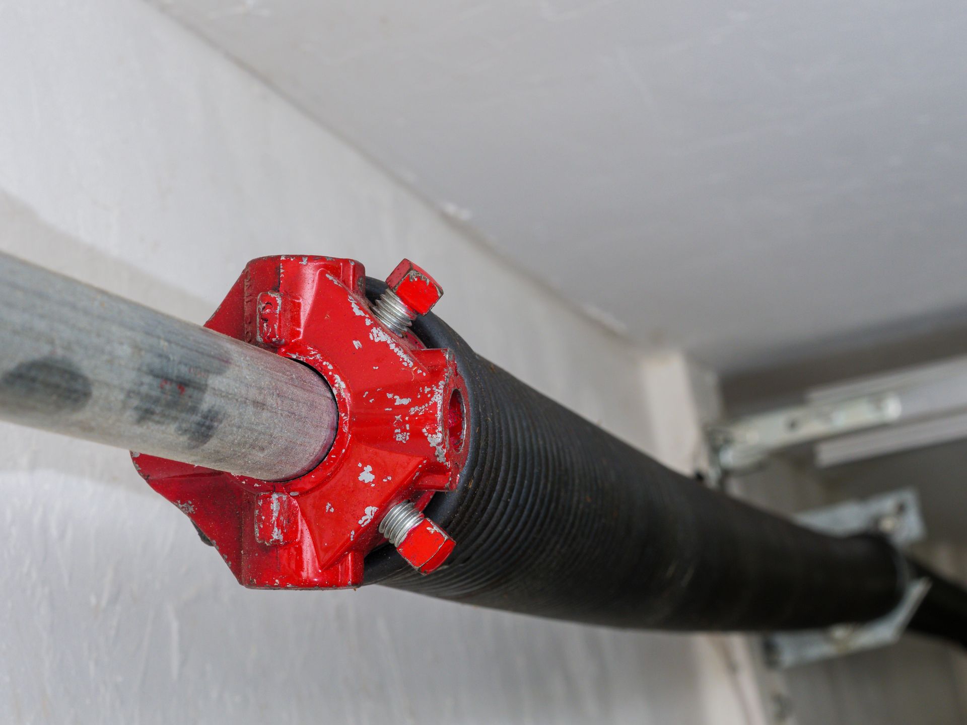 Red pipe coupling connecting a black insulated pipe to a gray pipe under a ceiling.