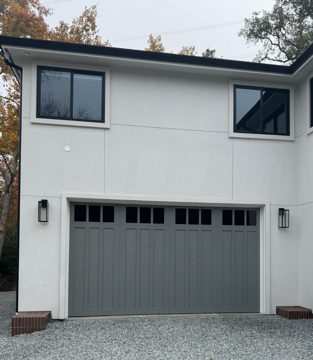 White two-story house with dark-framed windows and a gray double garage door